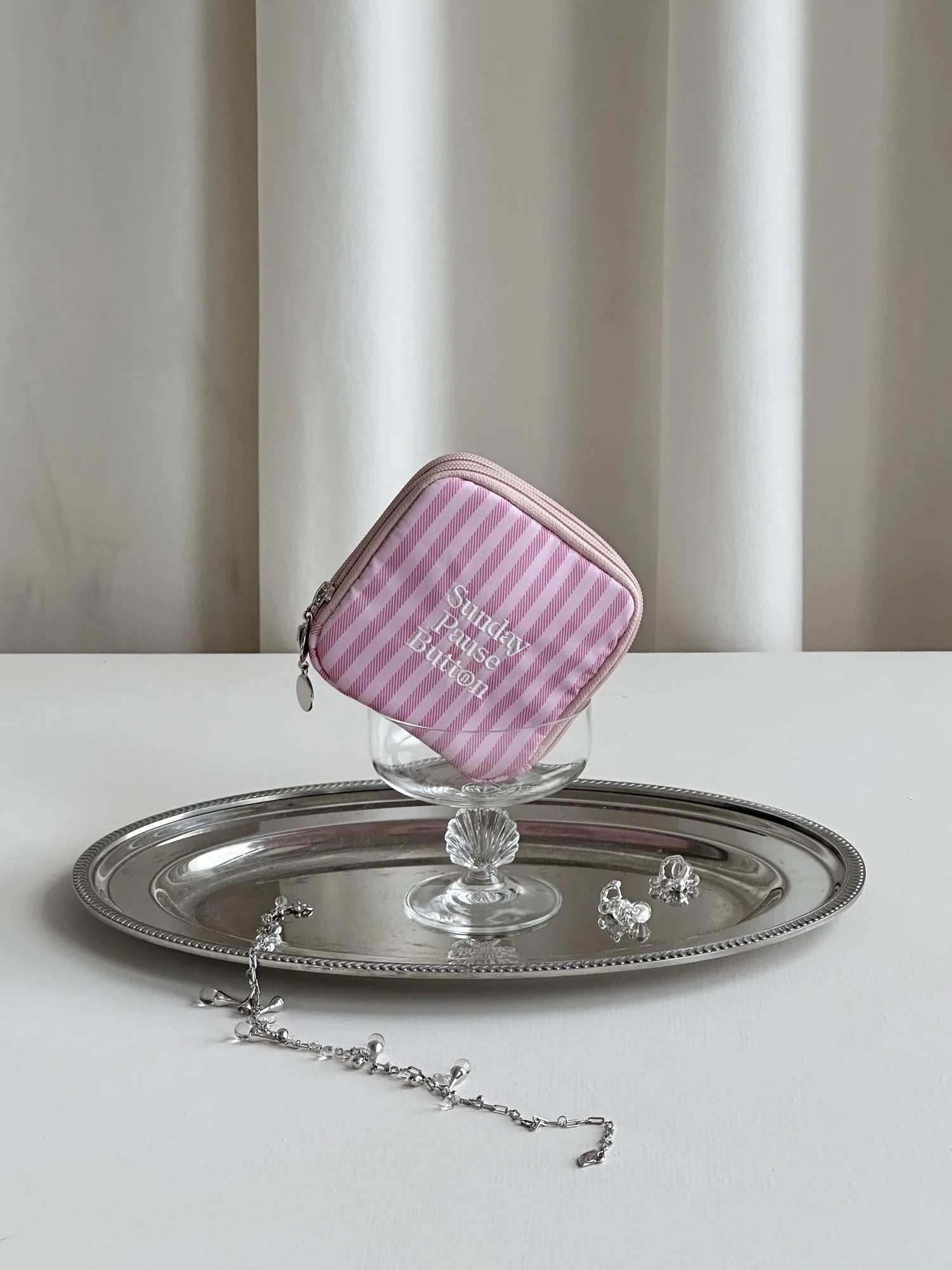 A pink striped pouch on a silver tray against soft curtains